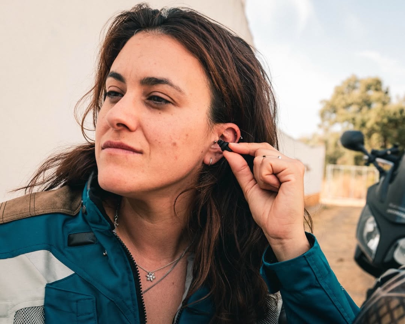 Creator fitting an earplug next to a motorcycle