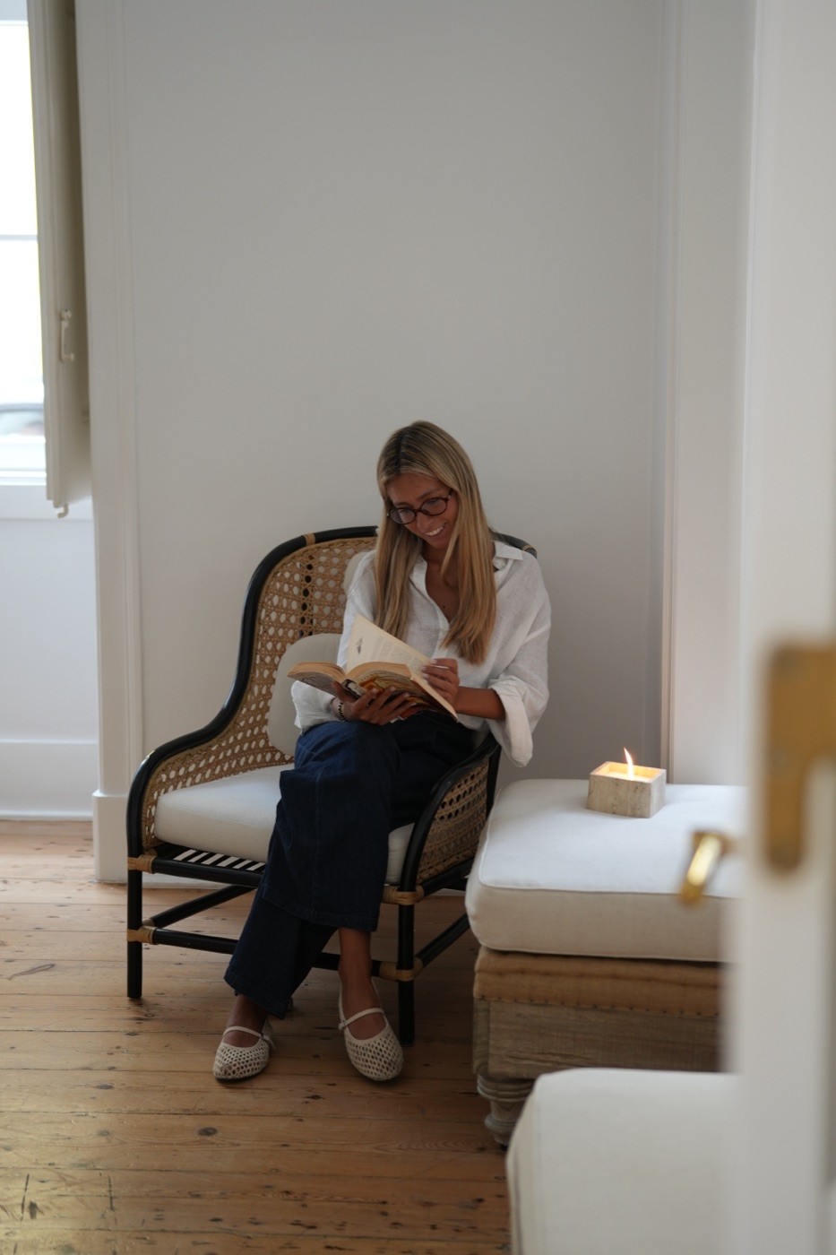 Creator reading in a rattan chair beside a candle